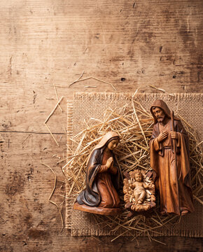 Overhead flat lay of a wooden nativity scene with baby Jesus, Mary, and Joseph on straw and burlap over rustic wood background