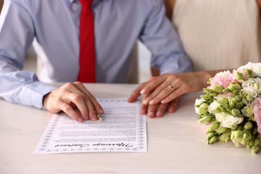 Couple signing marriage contract at light wooden table, closeup