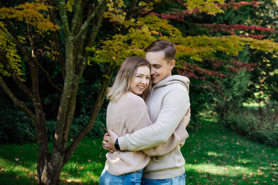 Portrait of young happy Caucasian couple in love hugging each other and enjoying the moment during romantic walk in nature in the fall park. Autumn mood. Youth feelings and first love concept