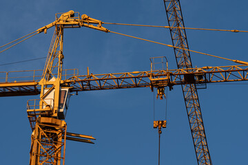 Tower construction cranes illuminated by warm golden hour sunlight against a deep blue sky at an urban building site. © Studio Aurelia