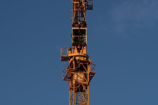 Close-up of a tower crane structure and operator cabin illuminated by warm evening sunlight against a clear blue sky.