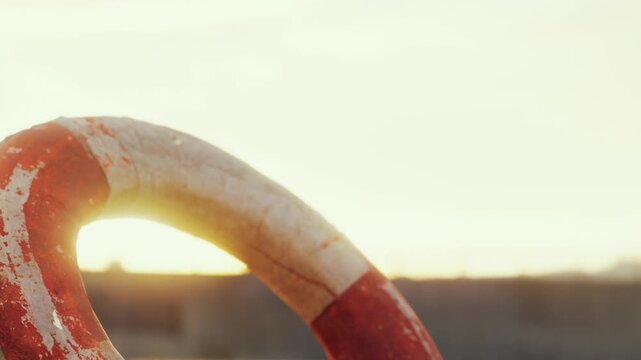 A vintage lifebuoy stands against a glowing sunset, casting soft shadows on the sandy shoreline. The scene reflects a tranquil moment by the ocean, evoking feelings of nostalgia and peace.