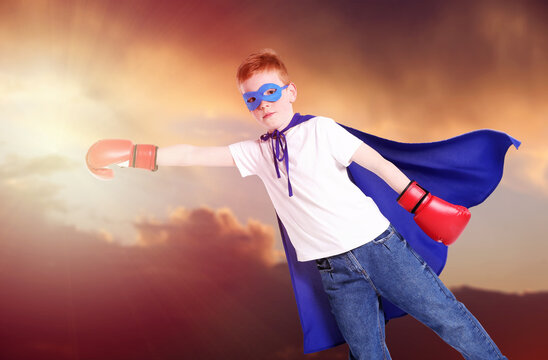 Little superhero. Boy with blue cape, mask and boxing gloves against sunset sky