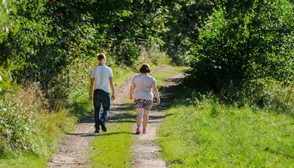 Two people walking along peaceful woodland trail in afternoon sunlight. © Trygve