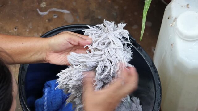 A woman checks the mop head after washing in a bucket