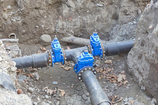 New blue gate valves installed on a triple pipeline utility junction in an excavation trench
