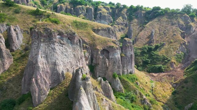 Drone footage of weathered rock cliffs and caves in southern Armenia, showing exposed rock layers, steep canyon walls, rocky terrain and mountain vegetation.