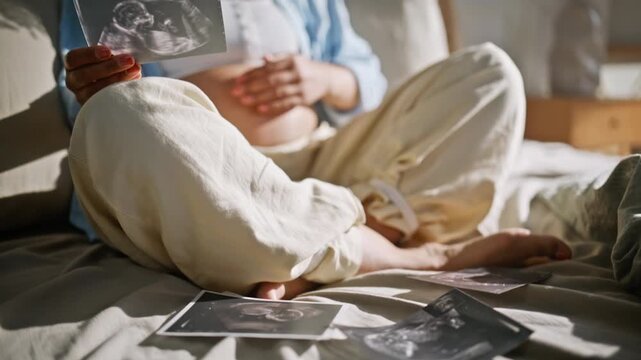 Expectant mother admiring sonogram bed. Curly woman caressing belly bedroom.