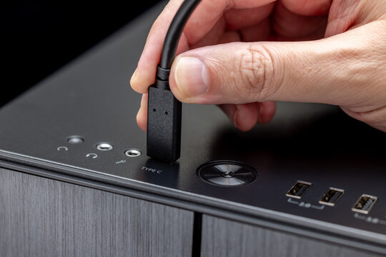 A hand connects a black cable to a TYPE C connector on a desktop PC case. On the black top panel, audio jacks, a round power button, and USB ports are visible