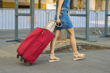 Woman Pulling Red Suitcase in city. Woman walking outdoors while pulling large red rolling suitcase and carrying handbag. Travel lifestyle, tourism, vacation, journey, transportation, luggage themes © svetlanais
