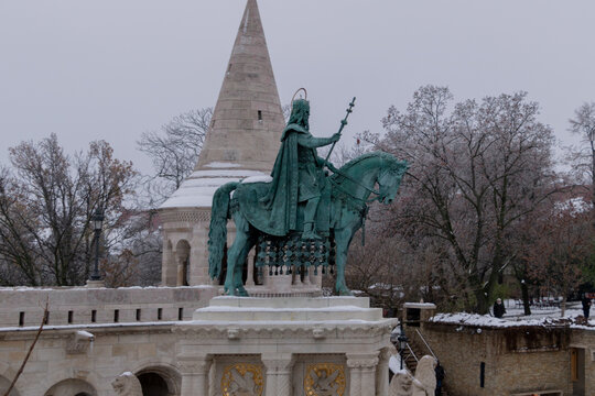 The majestic bronze equestrian statue of King Saint Stephen against a conical tower and snowy winter backdrop in Budapest.