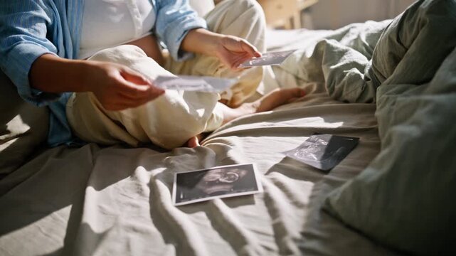 Closeup ultrasound photos bed. Happy pregnant woman examining sonogram bedroom.