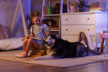 Childhood education and companionship, little girl reading a book to her husky dog in a cozy bedroom at night with soft evening lighting © Pixel-Shot