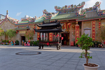 Fototapeta premium Courtyard of Wat Mangkon Kamalawat Chinese temple with large bronze incense burner and ornate dragon roof tiles in Bangkok, Thailand.