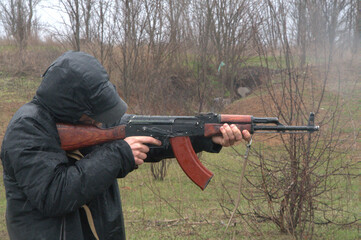 Fototapeta premium Person in black waterproof jacket and hood aiming rifle outdoors