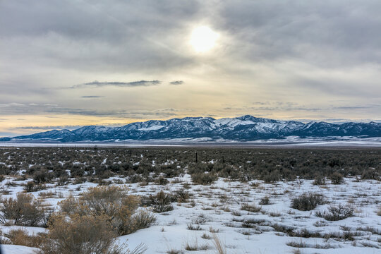 Overcast sun above snowy shrubs and distant mountains