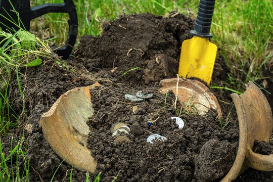 Excitement fills the air as a treasure hunter uncovers shiny coins and trinkets buried in the soft earth of a grassy garden. A sturdy shovel rests nearby, ready for more discoveries