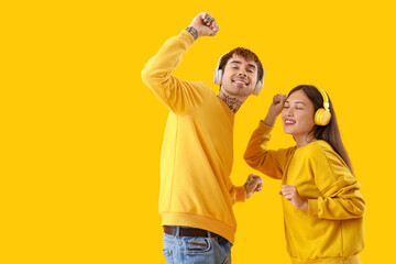 Obraz premium Young couple in headphones dancing on yellow background
