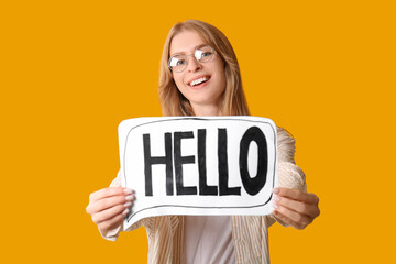 Beautiful woman holding paper speech bubble with word HELLO on yellow background © Pixel-Shot