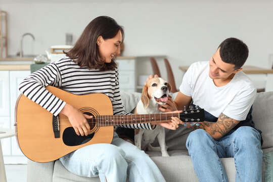 Young couple with cute Beagle dog playing guitar at home