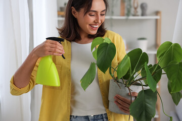 Young woman with plant and spray bottle at home