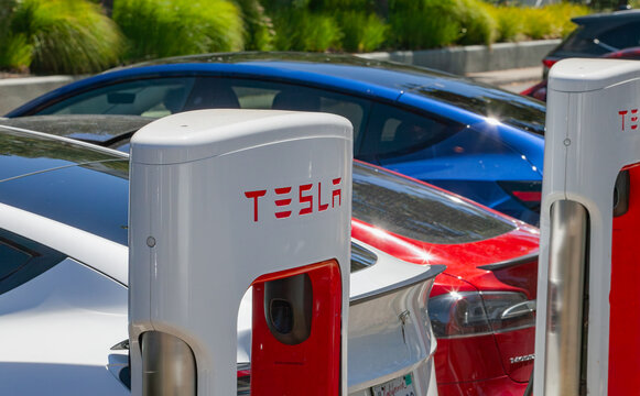Tesla Supercharger station with multiple electric vehicles parked and charging at an outdoor clean‑energy transportation facility