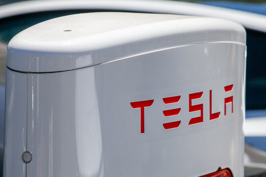 Close‑up of Tesla charging unit displaying red corporate lettering on white enclosure at contemporary electric‑vehicle charging site