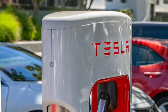 Close‑up of Tesla charging unit displaying red corporate lettering on white enclosure at contemporary electric‑vehicle charging site