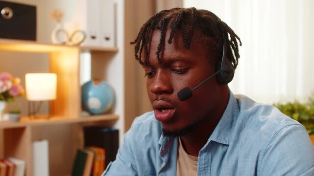African American young man on home table answers client in headset with calm support and guidance. Black guy on home table listens with focus explains solution and provides confident customer service.