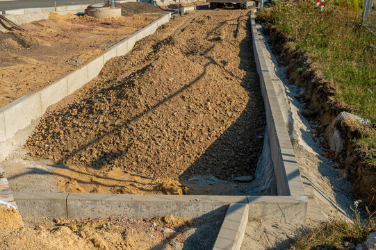 Road construction trench filled with soil and gravel bordered by concrete kerb stones. Ground preparation and earthwork for new pathway, pavement paving or sidewalk infrastructure project