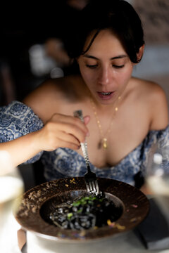 Woman eating squid ink pasta at a restaurant in Venice, Italy