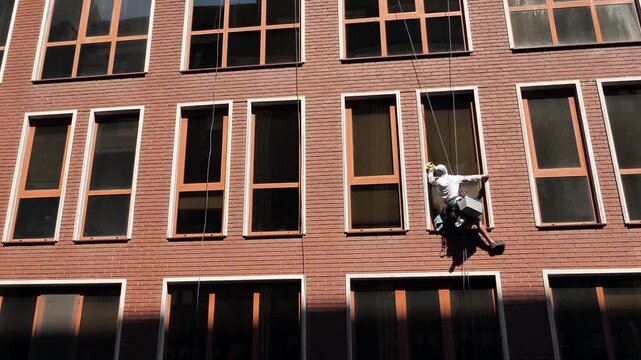 An industrial climber washes windows on the brick facade of a multi-story building.