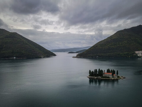 Our Lady of the Rocks island church in Perast, Montenegro, under a dramatic cloudy sky.