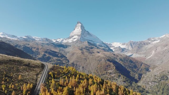 Aerial drone view of the Matterhorn mountain peak rising above a colorful autumn forest in Switzerland on a bright sunny day. Alpine autumn landscape.