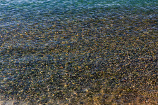 Crystal-clear water reflects sunlight over textured pebbles and sand