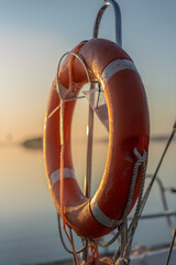 Orange Marine Life Buoy with Reflective Tape on Sailing Boat Railing at Sunrise © bartsadowski