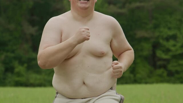 Fat man runs on grass. Outdoor fat jogging attempt. Fat body shows struggle. Fat loss motivation concept. Jogging man crosses green field. Beginner jogging shows effort. Overweight jogging.