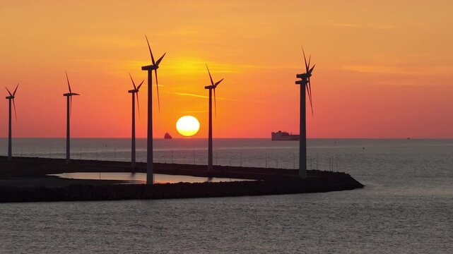 Drone view of wind turbines against a vibrant sunset. Silhouettes of wind turbines. Green renewable energy and wind farm technology at dusk.