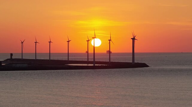 Drone view of wind turbines against a vibrant sunset. Silhouettes of wind turbines. Green renewable energy and wind farm technology at dusk.