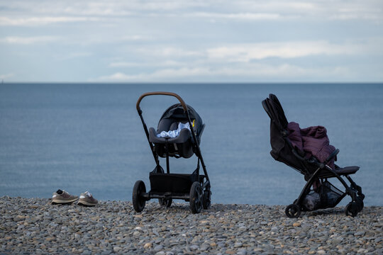 Two baby strollers on a pebble beach by the sea during a family vacation