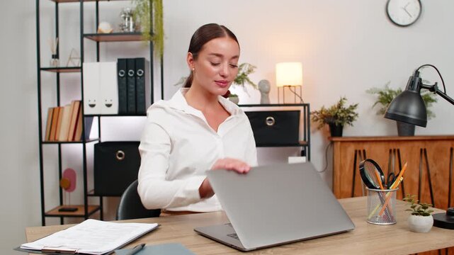 Young businesswoman at home office ends workday closes laptop smiles and feels relief after all tasks. Freelancer girl at table gives thumbs up breathes out and writes note done before leaving space.