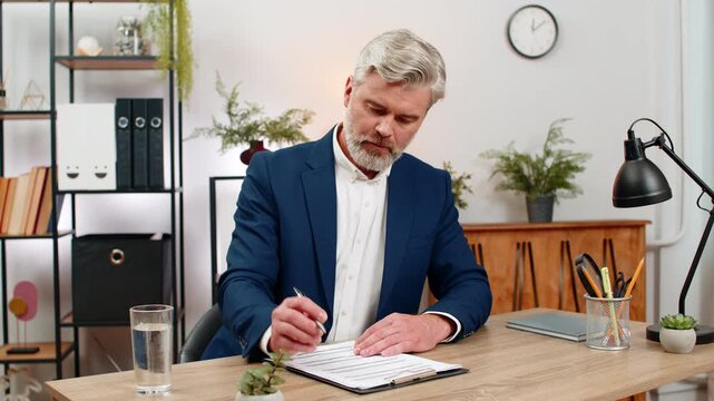 Middle-aged businessman at home office detects mistake in contract figures instantly correcting values with pen before signing. Freelancer guy at table updates ledger preventing fees building trust.
