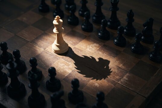 Single White Chess Queen Piece in Spotlight Casting Royal Crown Shadow Surrounded by Black Pawns on Wooden Board Leadership Power Strategy Concept