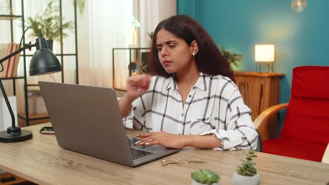Indian woman at home holds head staring at laptop baffled by complex task feeling stressed missing answer. Arabian girl at table shows confusion scrolling files on desk trying find solution quickly.