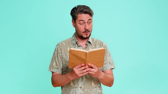 Middle-aged man reads book with focused expression, raised eyebrows, reacting to intriguing turn in plot or emotional moment. Young adult guy isolated on blue background engaged in reading literature.