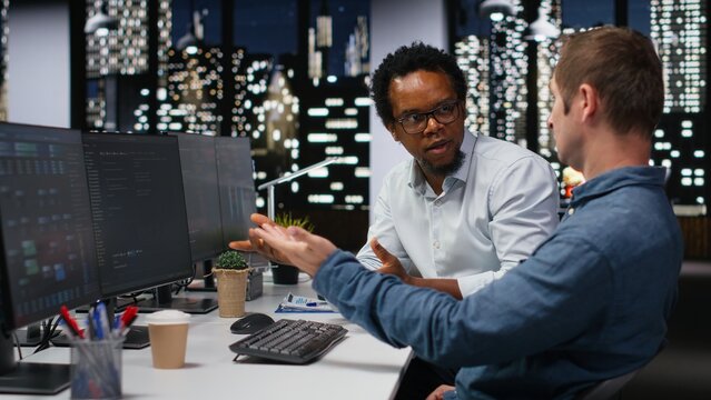 Technicians collaborate in an office, typing code on a computer and developing machine learning models to automate tasks while employees work together to write programming language scripts on a PC.