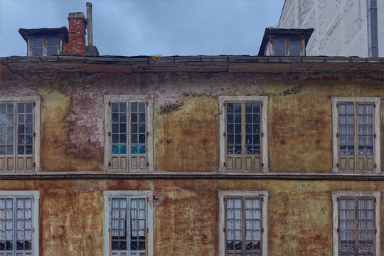 Dilapidated facade of a very worn three-story building featuring paint-faded wood windows divided by mullions and muntins. Luarca-Asturias-Spain-031