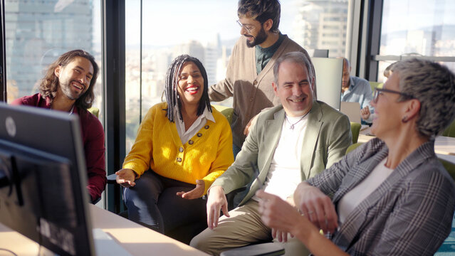 Diverse group of professionals laughing and talking during an informal meeting in a modern office. Bright corporate scene conveying teamwork, collaboration and positive workplace culture.