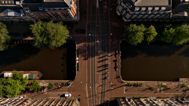 Straight-down drone view of cyclists crossing an Amsterdam canal bridge