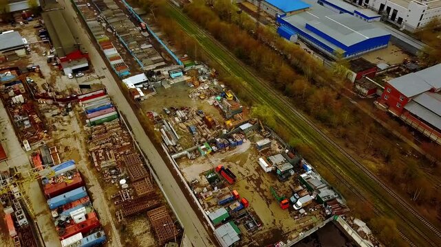 Aerial view of industrial zone with warehouse buildings, storage containers, scrap yards, and railway tracks in autumn